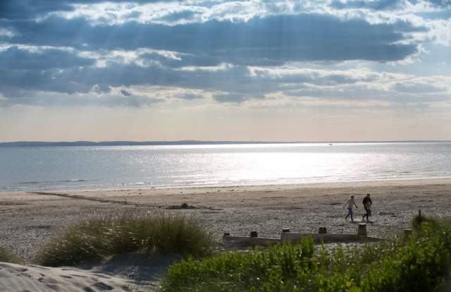 Sunny day at West Wittering beach looking out to sea, with a couple walking in the sandy dunes