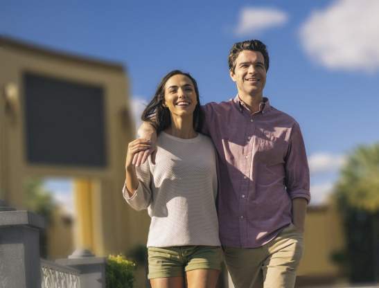 An hispanic couple embracing and walking in a theme park.