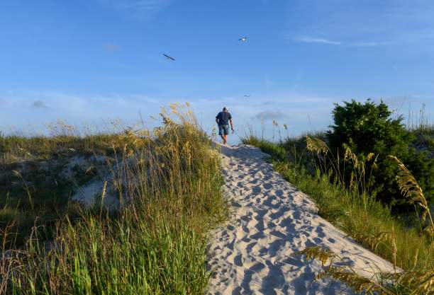 a man walking on a sandy beach path over the dunes on Oak Island, NC
