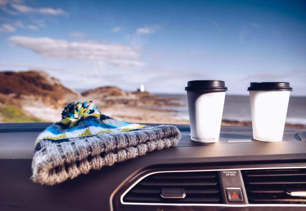 two coffee cups and a bobblehat on a car dashboard