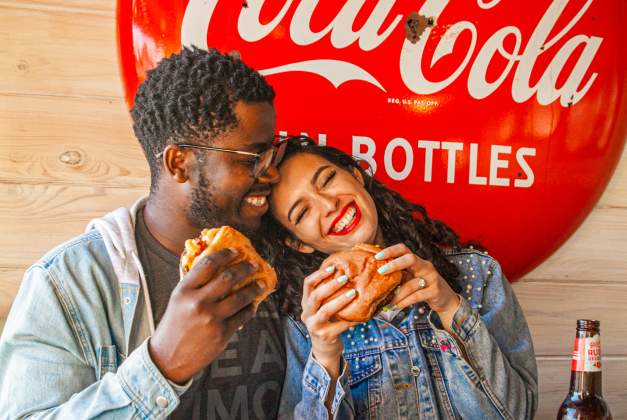 Couple eating burgers with a Coca-Cola sign behind them