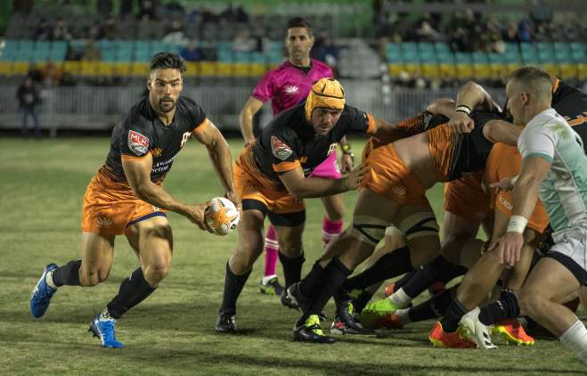 Austin rugby team, Austin Gilgronis, battling an opposing team while a player runs the ball towards the try zone.