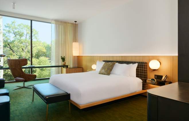 A hotel room with a bed, accent chair and large window at The Loren Hotel.