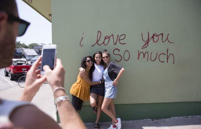 Girls posing at I Love You So Much Mural while friend takes photo