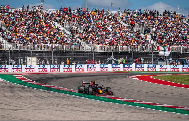 Formula 1 racecar rounding corner past crowd of cheering fans.