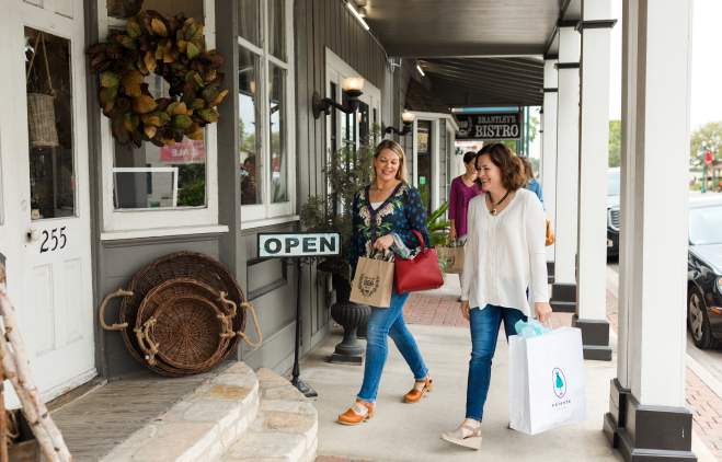 Two women facing each other and chatting as they walk off the sidewalk and into a boutique.