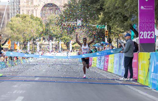 Image of a man crossing the finish line with his hands in the air at the Austin Marathon.