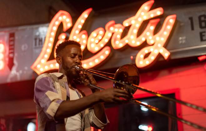 Austin musician Daniel Fears plays the trombone in front of The Liberty bar's lighted sign