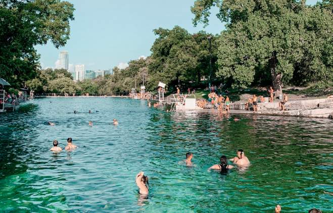 Adults and children playing in and along the banks of Barton Springs Pool.