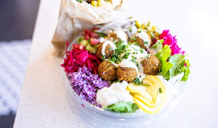 Falafel bowl with fresh vegetables, pickled cabbage, hummus and creamy sauce beside a wrapped sandwich