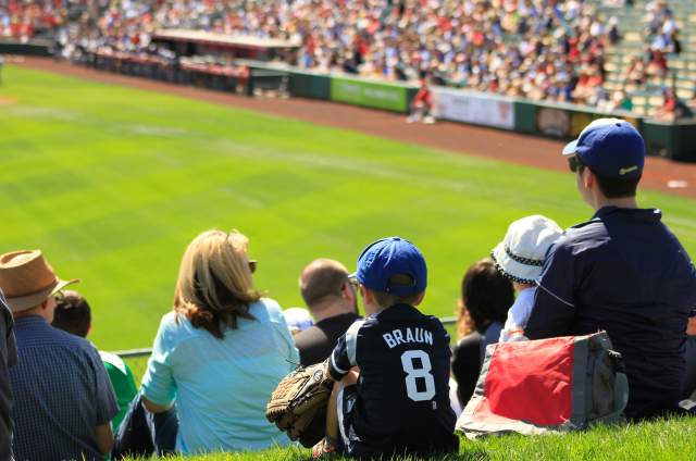Kid sitting in a crowd at a baseball game with jersey and glove on.