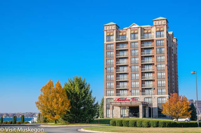 Hotel exterior on Muskegon Lake. The sky is blue and the trees have autumn color.