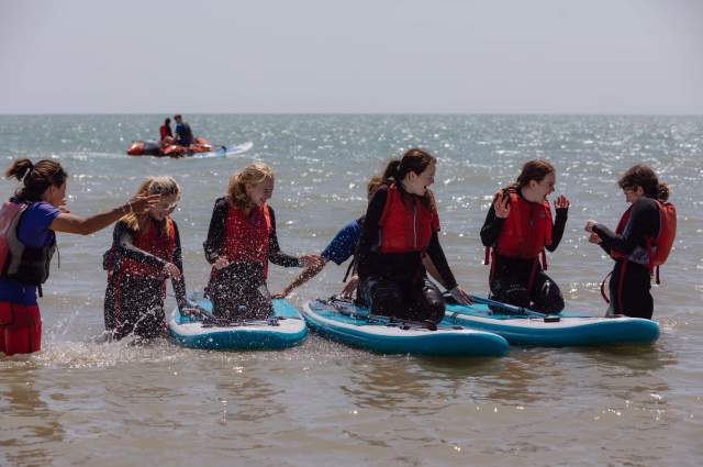 A group of young people wearing red life vests sit on paddleboards in the sea at Eastbourne