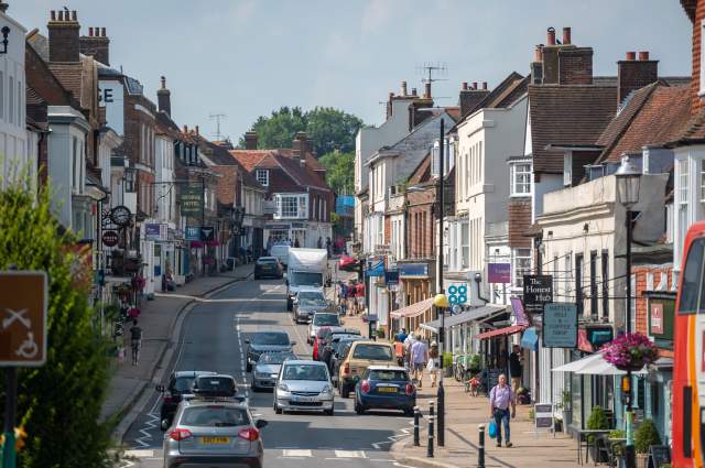 A busy high street with traffic in the historic town of Battle, Sussex, with shop fronts and shoppers