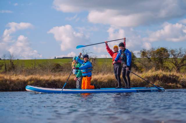 A group of paddleboarders sit and stand on their board in the river in the South Downs National Park