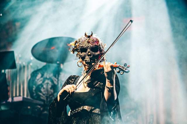 A performer from The Rock Orchestra plays the violin while wearing a gruesome skeleton mask