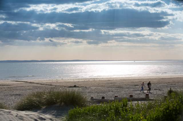 Sunny day at West Wittering beach looking out to sea, with a couple walking in the sandy dunes