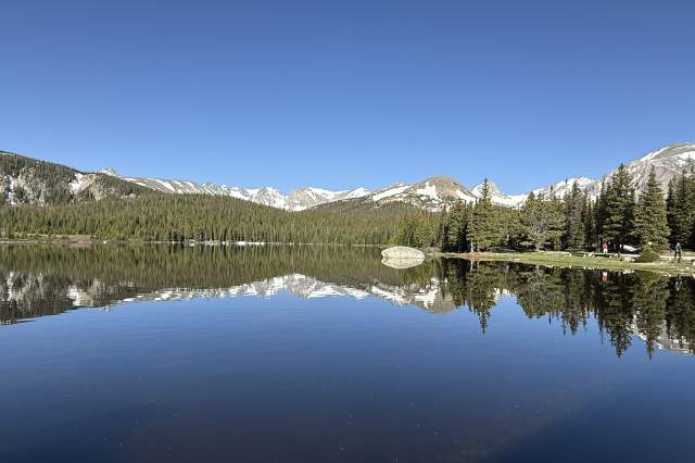 A mountain ridge line and blue sky is reflected in a still Brainard Lake