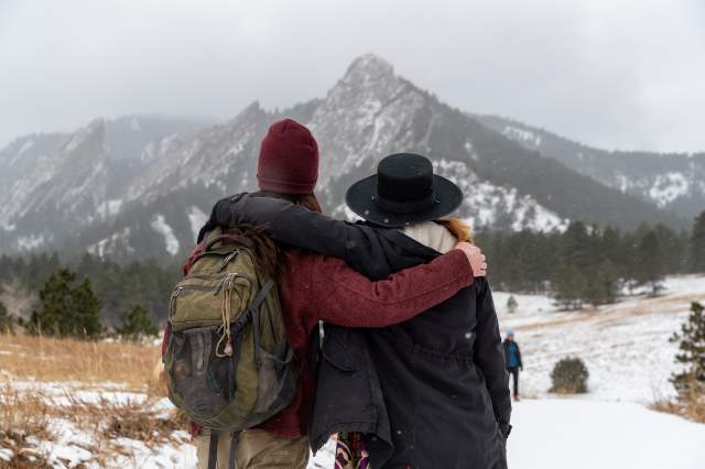 Two hikers with their arms around one another looking at the snow covered Boulder's Flatirons