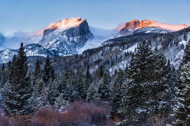 The first golden light of day hit Hallett Peak and Flattop Mountain with fresh snow on the trees, seen from the Storm Pass trailhead, Rocky Mountain National Park, Colorado.