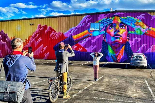 A woman poses in front of a colorful mural on JD's Joyrides Mural Tour in Boulder.