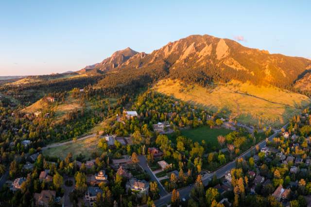Aerial view of Boulder, Colorado looking west to the Flatirons with reddish sunlight on the mountains and clouds