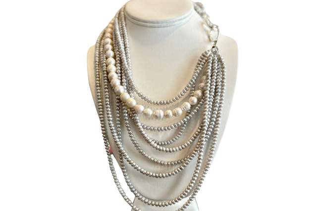 A display of various layered pearl and silver necklaces on a white bust mannequin.
