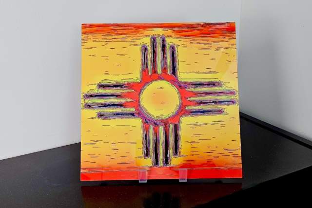 A painting of the Zia Sun symbol, displayed on a stand, featuring a yellow circle center with rays radiating outward set against a vibrant yellow and orange background.