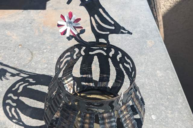 a sculpted metal candle holder with a caricature of a quail next to a flower sits on a stone bench