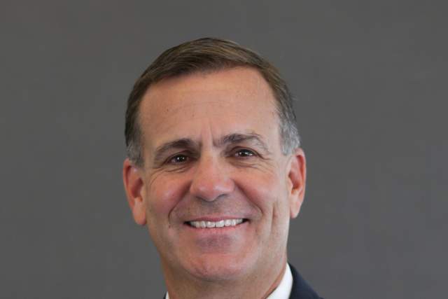 Headshot of Mark Harlan wearing a dark suit and red tie with a University of Utah pin on his lapel