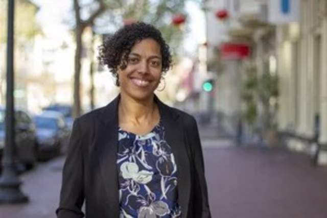 Woman wearing a flowered shirt and black suit coat standing on a city sidewalk