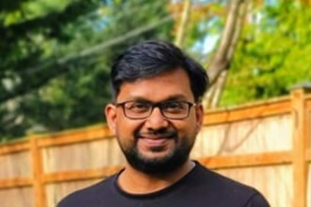 A man standing in front of a fence wearing a black t-shirt