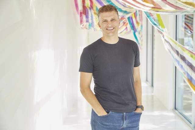 Smiling man in black t-shirt and jeans standing in front of colorful drapes