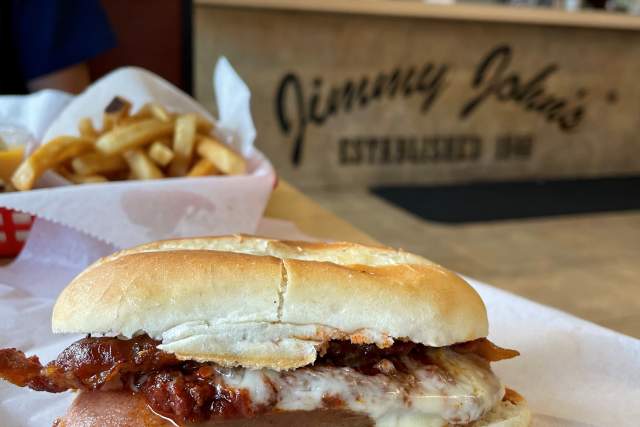 A chili dog set on a table in front of a sign that reads Jimmy John's