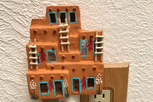 A night light resembling traditional Puebloan architecture plugged into an electrical socket with a wooden border on a white wall