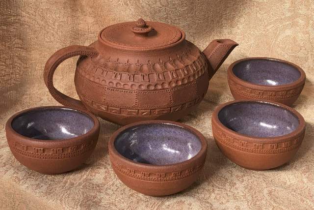 red clay engraved bowls and a tea kettle sit on a brown cloth background