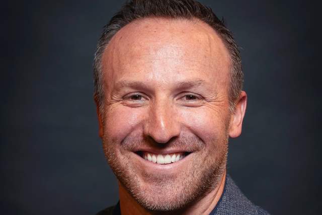 Smiling man in grey blazer and dark blue polo shirt