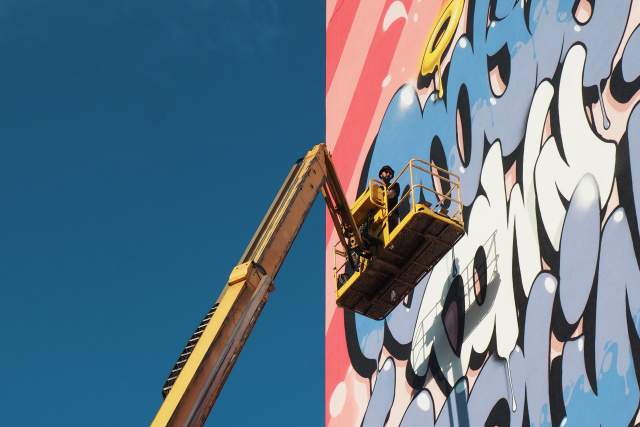 mural painter on cherry picker painting on side of building