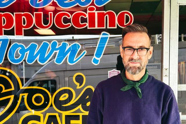 Smiling man standing in front of a cafe window with words on it