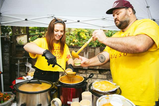 A man and woman in matching yellow shirts scooping queso into little cups at Quesoff 2023.