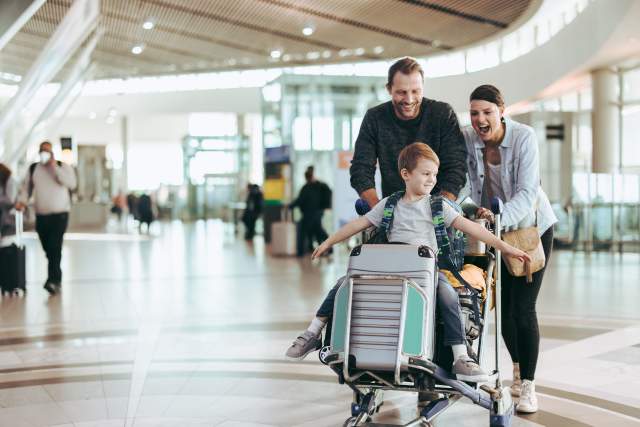Couple happily pushing the trolley with their son at airport.