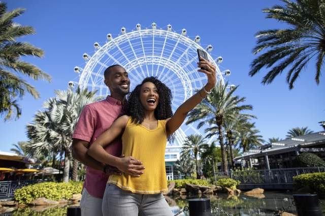 A couple posing for a selfie in front of The Wheel at ICON Park