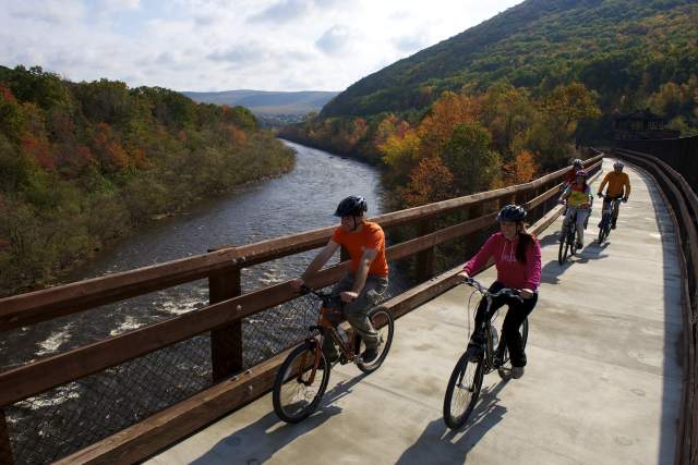 Family bikes across a bridge with mountains and a river in the background