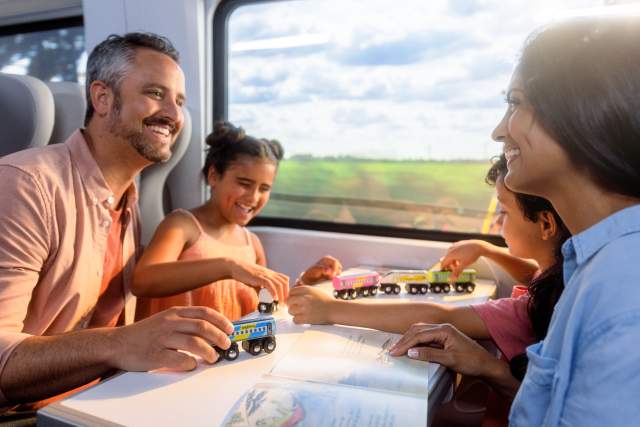 Family riding on Brightline train while kids play with toy train