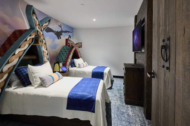 Two beds with carved wooden headboards, a dragon wall mural, and rustic wooden elements in the How to Train Your Dragon Kids Suite at Universal Helios Grand Hotel, a Loews Hotel