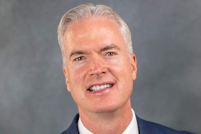 Smiling man in dark blue suit with white button up shirt and light blue tie