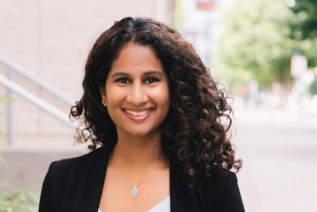 Smiling woman standing on a sidewalk wearing a black jacket and white shirt