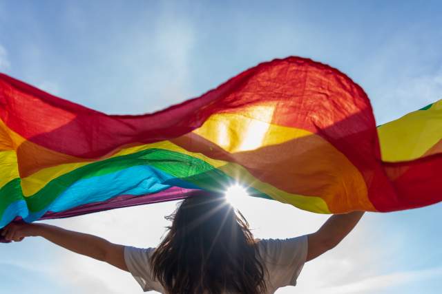 Picture of a young woman waving lgbti flag under the sky