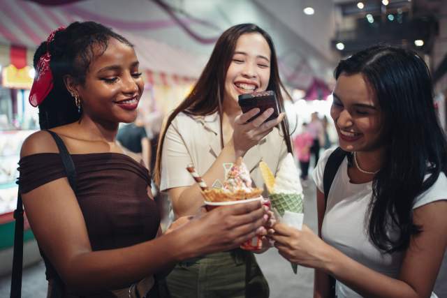 Happy girlfriends capturing a photo of their ice cream in the city at night.