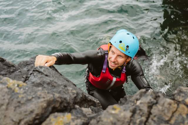 Coasteering adventure in Swansea Bay with a man dad climbing rocks from the sea in safety gear